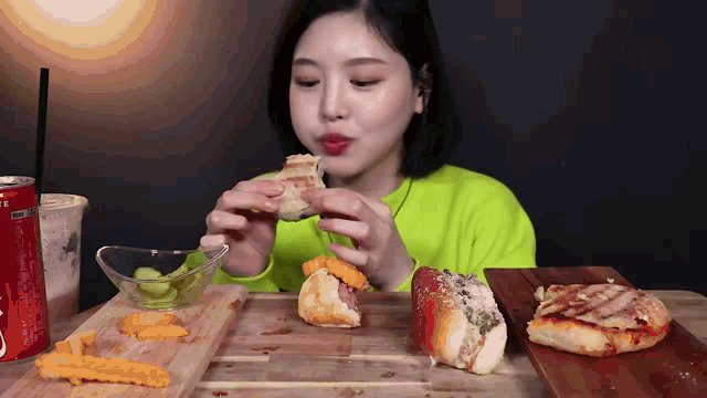 a woman in a neon green shirt is eating a sandwich next to a coca cola can