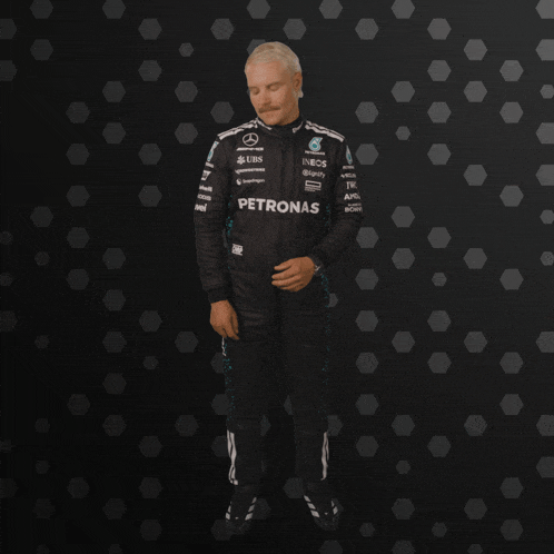 a man in a petronas racing suit stands in front of a black background