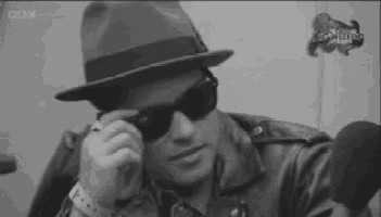 a man wearing a hat and sunglasses is sitting in front of a microphone