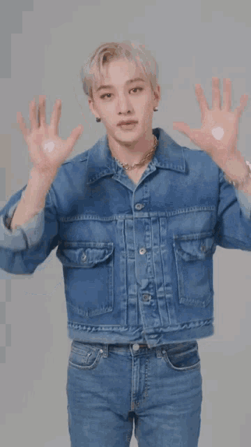 a man wearing a denim jacket and jeans is holding his hands up