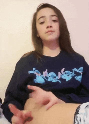 a girl wearing a blue sweatshirt with stitch on it is touching her belly