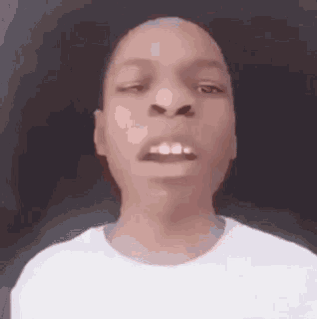a young man in a white t-shirt is making a funny face with his mouth open .