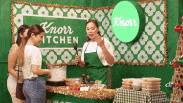a woman in a green apron stands in front of a knorr kitchen sign