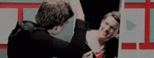 two men are standing next to each other in front of a mirror . one of the men is wearing a tie .
