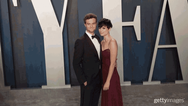 a man in a tuxedo and a woman in a red dress pose for a picture in front of a large y and a