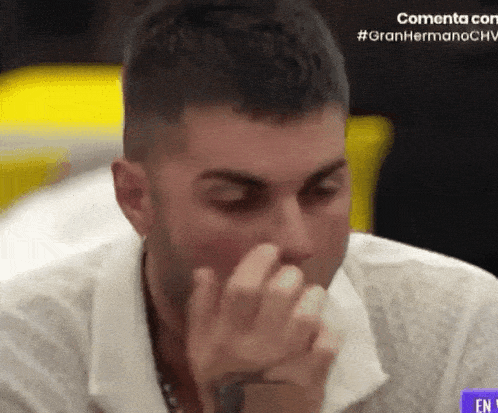 a man covering his mouth with his hand in front of a sign that says commenta con #granhermanochv