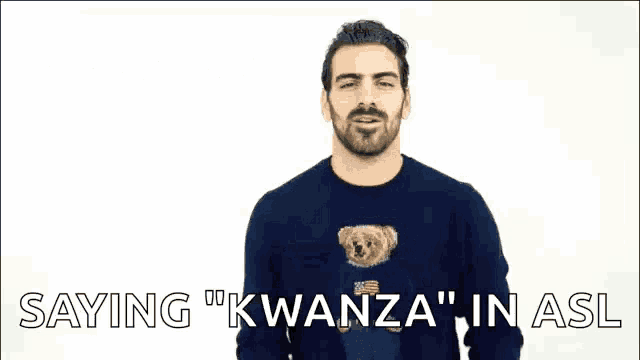a man with a beard wearing a polo bear sweater is saying " kwanza " in asl
