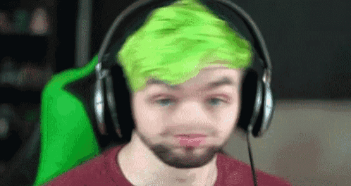a man with green hair is wearing headphones and making a funny face .
