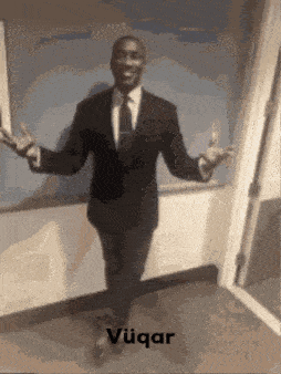 a man in a suit and tie is standing with his arms outstretched in front of a wall with the word vuqar written on it