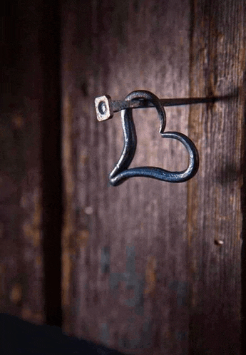 a wrought iron hook in the shape of a heart is hanging on a wooden wall .
