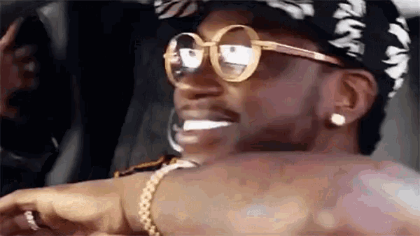 a man wearing sunglasses and a bandana is smiling while sitting in a car .