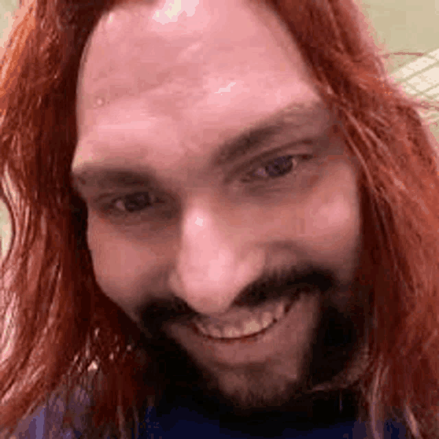 a close up of a man with long red hair and a beard smiling .