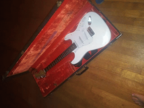 a white guitar in a red case with a signature on the neck