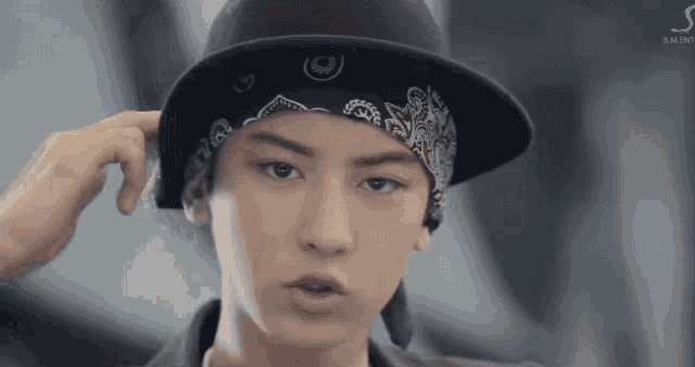 a young man wearing a bandana and a hat is looking at the camera