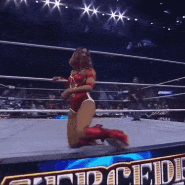 a female wrestler is kneeling down in a wrestling ring with the word pride behind her