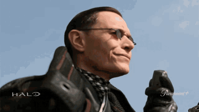 a man wearing sunglasses and a halo jacket is holding a cellphone