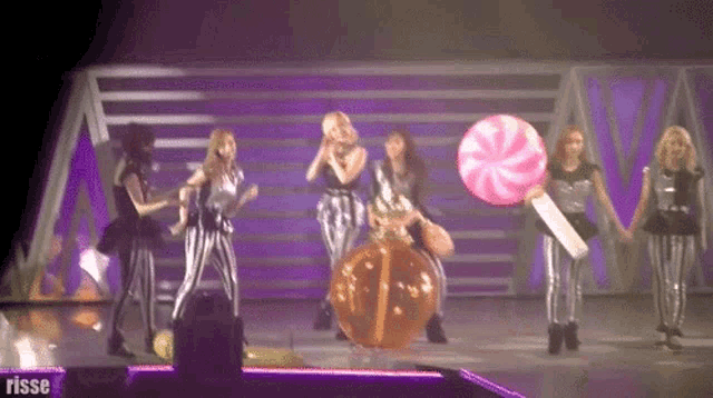 a group of women are dancing on a stage with a purple background and the word rosse on the bottom right
