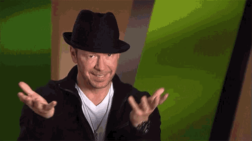 a man wearing a black hat and a white shirt is smiling with his hands outstretched