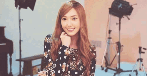 a woman in a polka dot dress is smiling in a room with a piano and a camera .