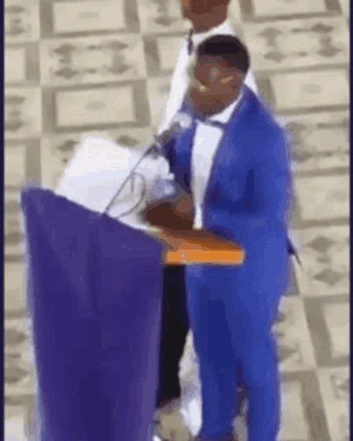 a man in a blue suit is standing at a podium holding a bible .