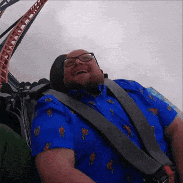 a man wearing glasses and a blue shirt is smiling while riding a roller coaster