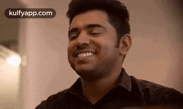 a man in a black shirt is smiling with his eyes closed and his mouth open .