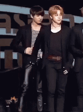 two men are standing next to each other on a stage . one of the men is wearing a striped shirt .