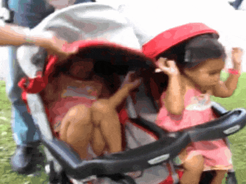 two little girls are sitting in a stroller with a red canopy