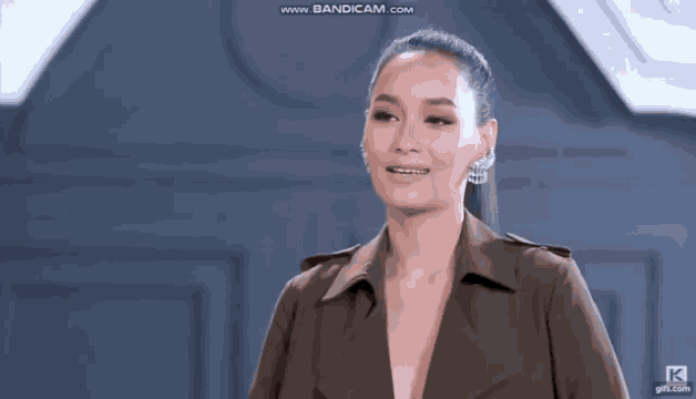 a woman in a trench coat is smiling and wearing earrings