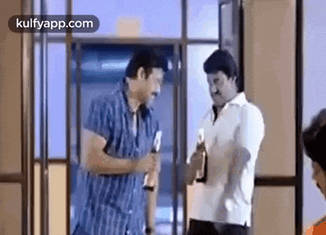 two men are standing next to each other in a room talking to each other while holding bottles .