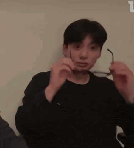 a young man in a black shirt is holding a pair of glasses in his hands .