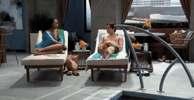 a man and a woman are sitting on lounge chairs near a swimming pool