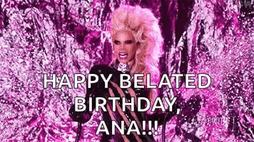 a drag queen is standing in front of a pink background and says `` happy belated birthday , ana !!! ''