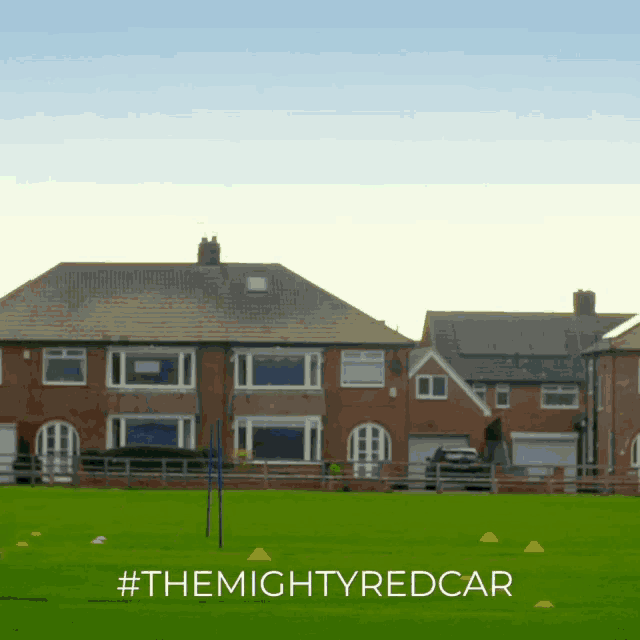 a field with houses in the background and #themightyredcar written on the bottom