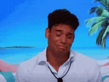 a man in a white shirt is crying with a palm tree in the background