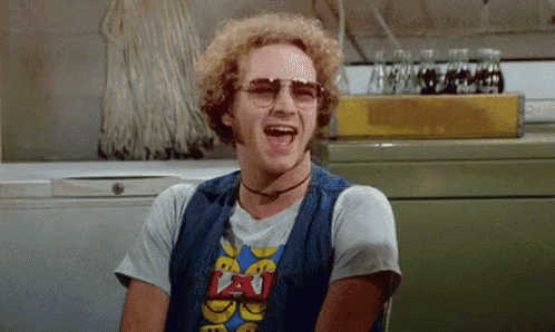 a man wearing sunglasses and a t-shirt with the word peace on it is laughing with his mouth open .