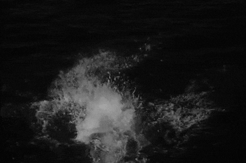 a black and white photo of a wave crashing on a rock in the ocean .