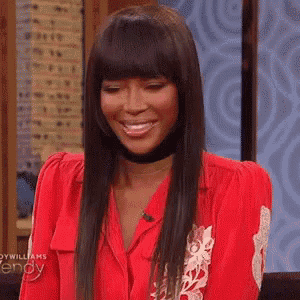 a woman wearing a red shirt and a choker is smiling on a television show .