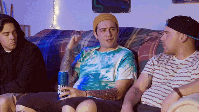 three men are sitting on a couch with a can of bud light