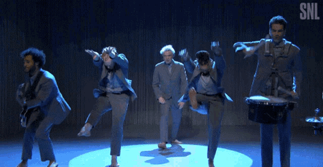 a group of men are dancing on a stage with the snl logo in the corner