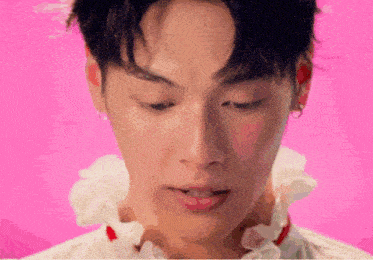 a close up of a young man 's face with a pink background and a white collar .