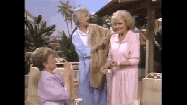 three women are standing next to each other on a porch . one of the women is holding a fur coat .