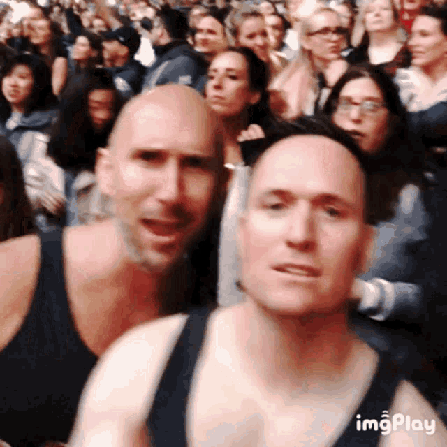 a man in a black tank top stands in a crowd of people with imgplay written on the bottom