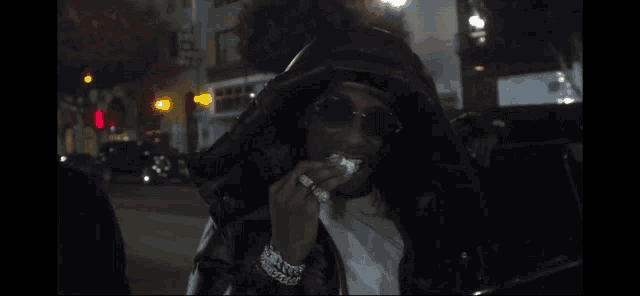 a woman wearing a hooded jacket and sunglasses eating a piece of food