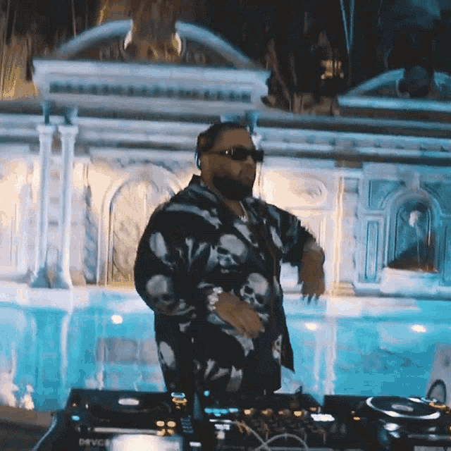 a man wearing sunglasses and a skull shirt is playing music in front of a swimming pool