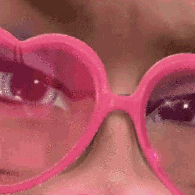 a close up of a woman wearing pink heart shaped glasses .
