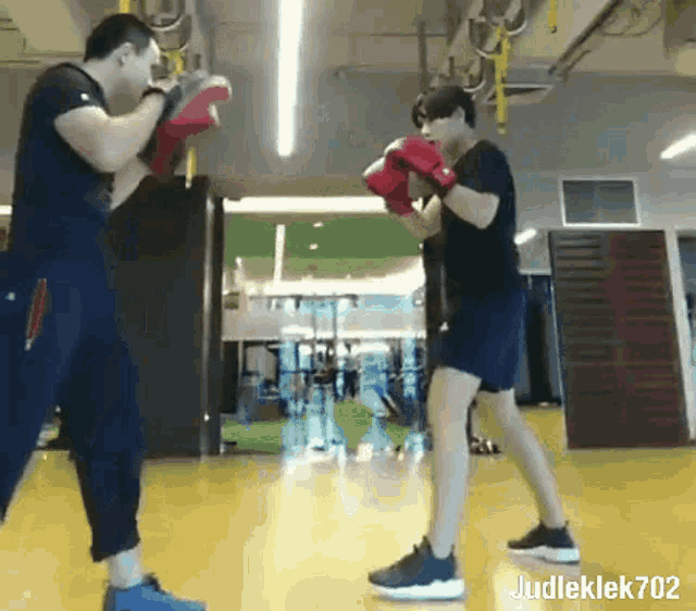 a man wearing boxing gloves is standing next to another man in a gym .
