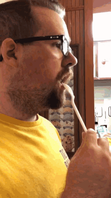 a man wearing glasses and a yellow shirt is eating a popsicle