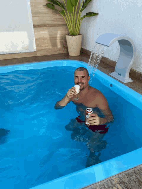 a man is sitting in a pool holding a glass and a can of soda