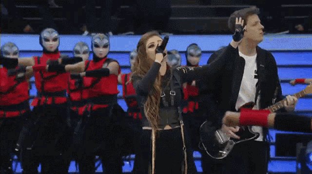 a woman singing into a microphone while a man playing a guitar stands behind her